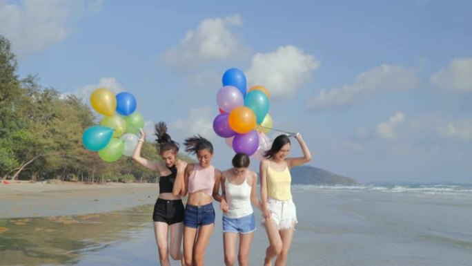 一群女朋友带着气球在蓝天的背景下在海滩上散步。幸福的朋友在夏日阳光明媚的阳光下在海滩上玩耍。假期-i