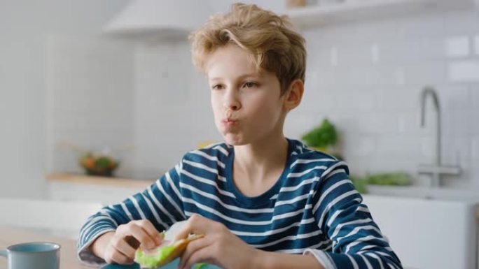 可爱的小男孩在厨房餐桌上吃三明治的肖像。帅哥吃一口健康零食