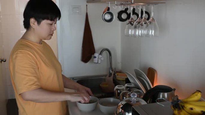 一位亚洲中国中年妇女喜欢早上在厨房准备早餐，一边听耳机