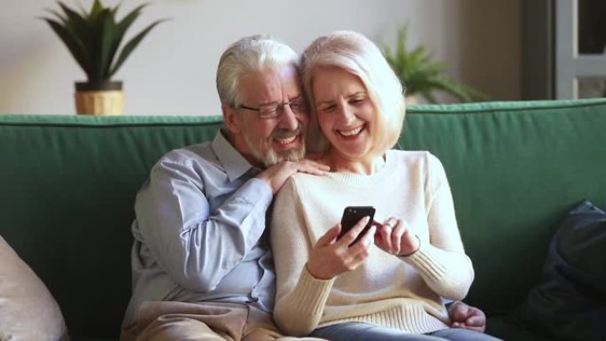 老妻子和丈夫坐在沙发上使用智能手机应用程序