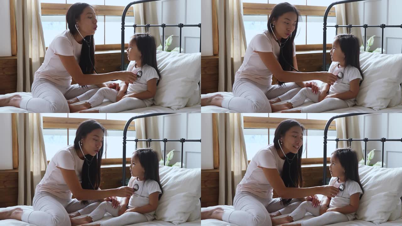 快乐的亚洲妈妈和孩子女儿在床上玩医生