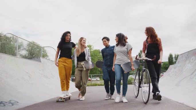 带滑板和自行车的女性朋友走过城市滑板公园