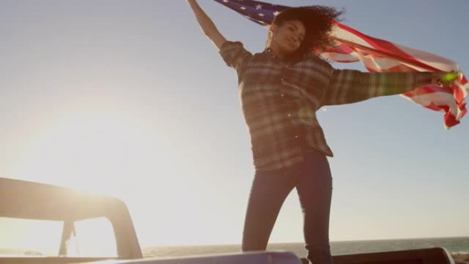女人在4k海滩的皮卡车上挥舞着美国国旗