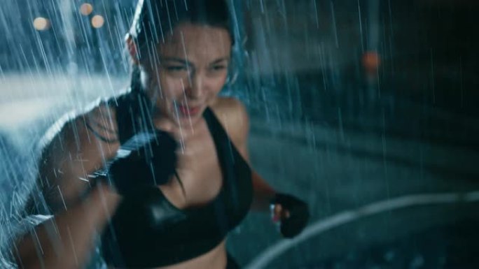 美丽的运动健身女孩正在做拳击运动。她晚上在大雨中锻炼身体，身后有一盏灯。