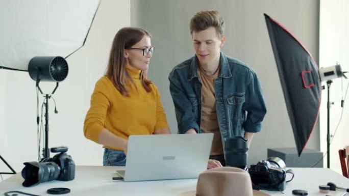 开朗的年轻人男人和女人在使用笔记本电脑在工作室观看照片