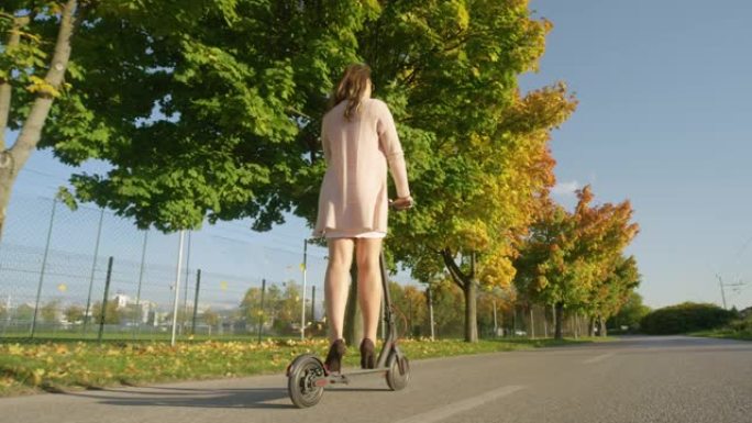 低角度: 女性通勤者沿着秋天的彩色大道骑电动踏板车