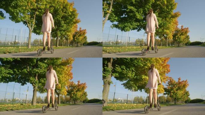 低角度: 女性通勤者沿着秋天的彩色大道骑电动踏板车