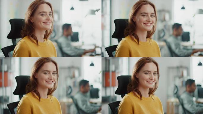 穿着黄色毛衣的红头发的美丽年轻女子的肖像与同事聊天，对着镜头微笑着转身。在明亮多样的办公室工作的成功