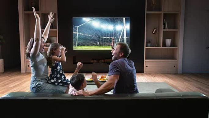 一家人正在电视上观看足球时刻并庆祝进球