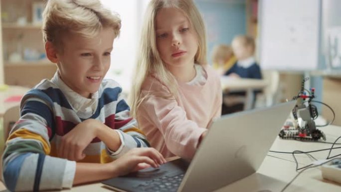 出色的女学生和男生交谈并使用笔记本电脑为机器人工程课程编程软件。小学科学教室，孩子们从事技术工作。S