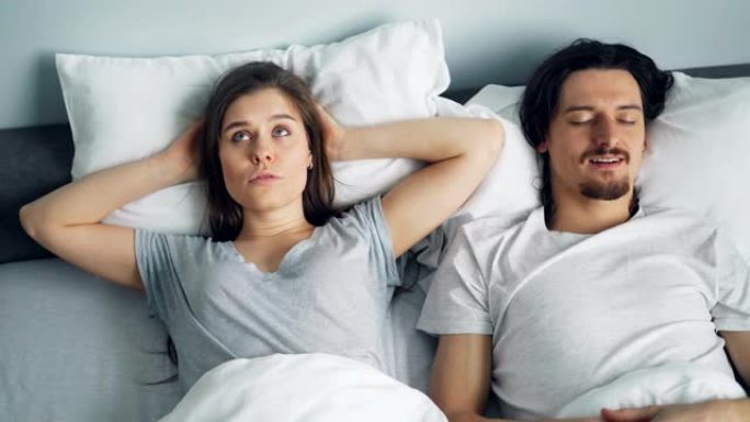 丈夫在床上打鼾时，不幸的女孩用枕头遮住耳朵