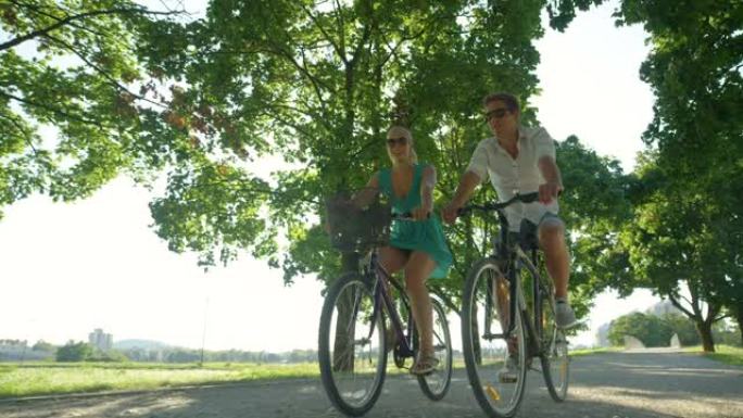 低角度: 阳光照射在公园周围骑自行车的快乐旅游夫妇身上