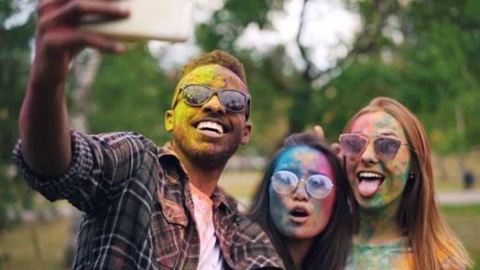 快乐的人的慢动作多种族群体在派对上自拍，脸和头发都是彩色的。男人和女人都戴着墨镜和脏衣服。