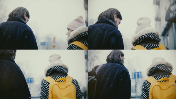 后视图快乐放松的年轻浪漫情侣穿着休闲暖和的衣服走在一起，在一个白雪皑皑的寒冷的冬日亲吻。