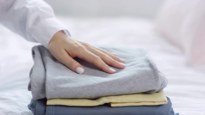 女人的手坐在床上，触摸折叠的衣服