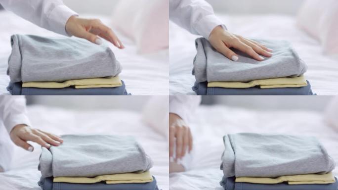 女人的手坐在床上，触摸折叠的衣服