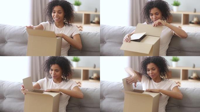 快乐非洲女人顾客打开纸箱坐在沙发上