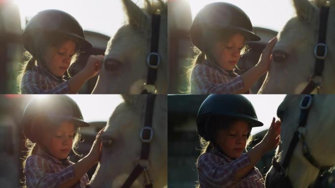 真实的近距离拍摄一个可爱的小女孩戴着骑师头盔，是爱抚着一匹白马在骑马厩与阳光