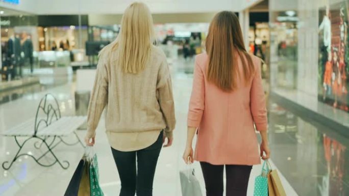 苗条的年轻妇女在购物中心里拿着纸袋走着，环顾四周。快乐的顾客，闪亮的商店橱窗可见。