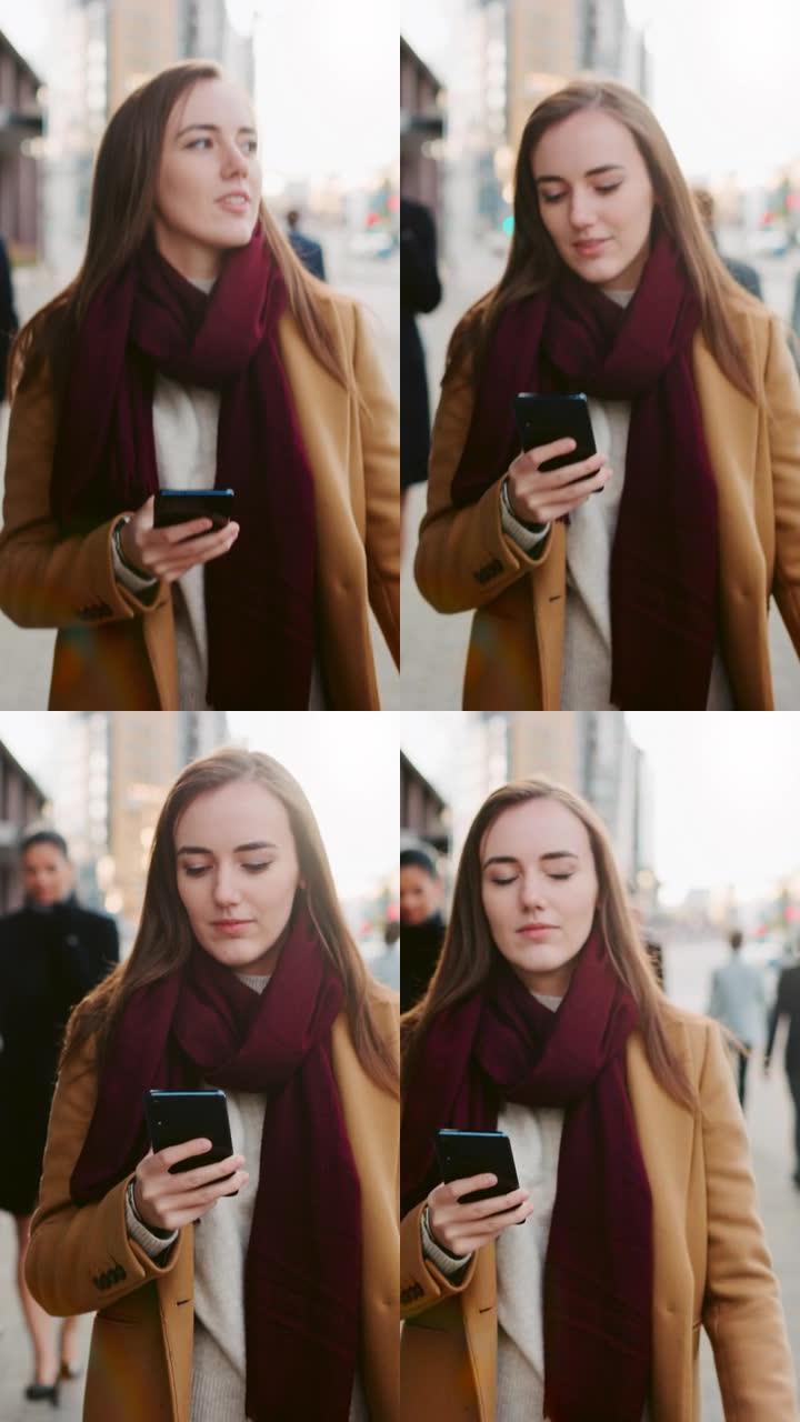 穿着棕色外套的美丽女商人正在市中心的街道上使用智能手机。她走在拥挤的步行街上，看起来很成功。垂直屏幕