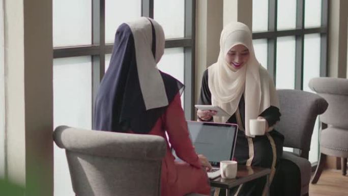 两个穆斯林人在咖啡店里用平板电脑和笔记本电脑工作和讨论。