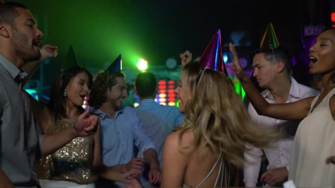 美丽的生日女人在酒吧里戴着生日帽子在朋友之间跳舞