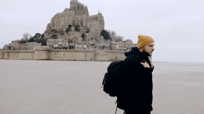 快乐兴奋的欧洲旅游男子背着背包离开诺曼底史诗圣米歇尔山城堡慢动作