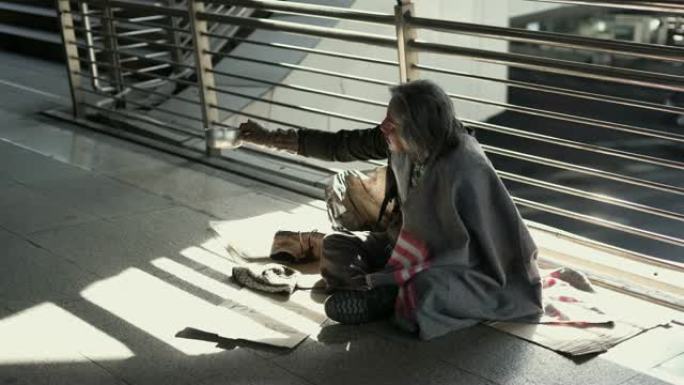 无家可归的人在人行道上拿着乞讨碗。