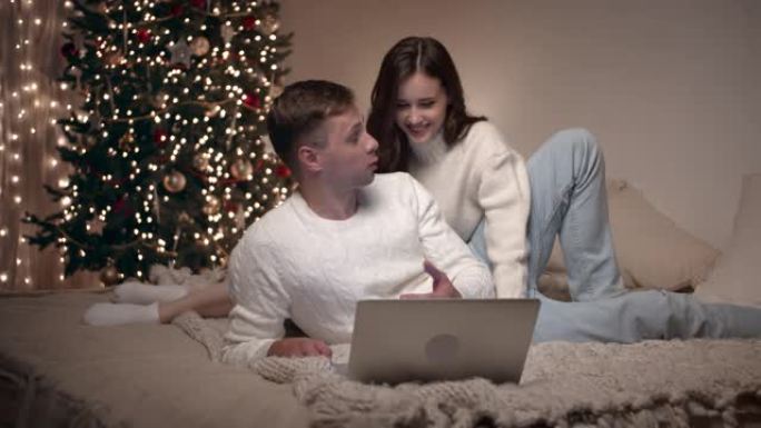 年轻夫妇坐在床上看卧室里的圣诞照片。