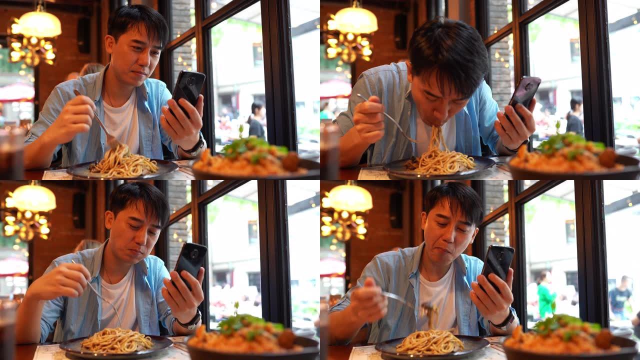 亚洲青年男子一边吃面条一边看手机