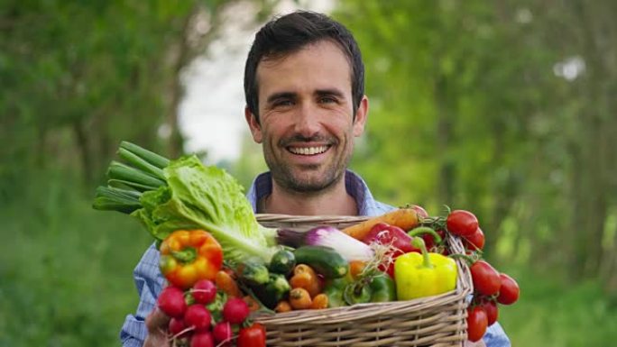 一个快乐的年轻农民在篮子里拿着新鲜蔬菜的肖像。在自然的背景下。
