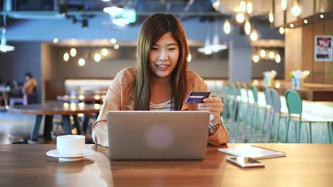 4k镜头亚洲妇女使用信用卡与笔记本电脑在共同工作空间，商务和在线支付概念进行在线交易的场景