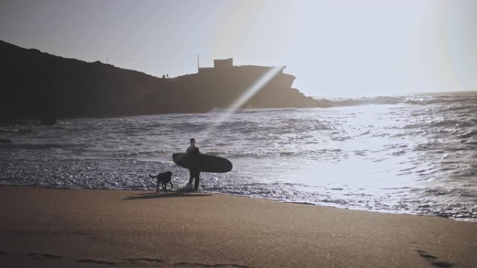 海滩海岸边带着狗抱着冲浪板的老人