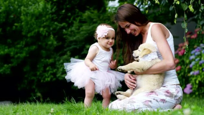 在一个阳光明媚的春天，一个打扮成芭蕾舞演员的小女孩在花园里和她的妈妈和金毛猎犬小狗玩耍，每个人都像一