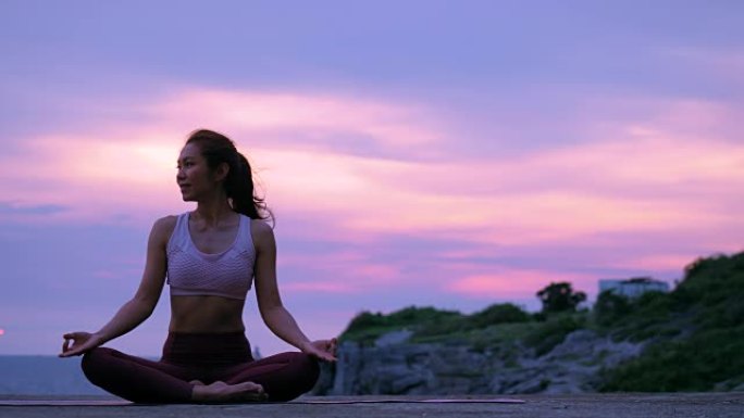 快乐的年轻女子在日落时在海滩上练习瑜伽放松，日出背景。健身、运动、瑜伽和健康生活理念。