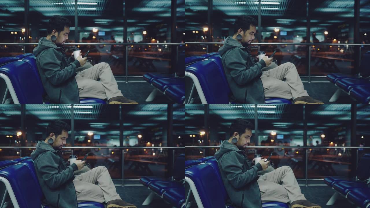 商人坐在机场，晚上使用手机。