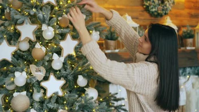漂亮的年轻女子正在装饰圣诞树，触摸球和玩具，微笑着享受节日和节日活动。新年传统和青年观念。
