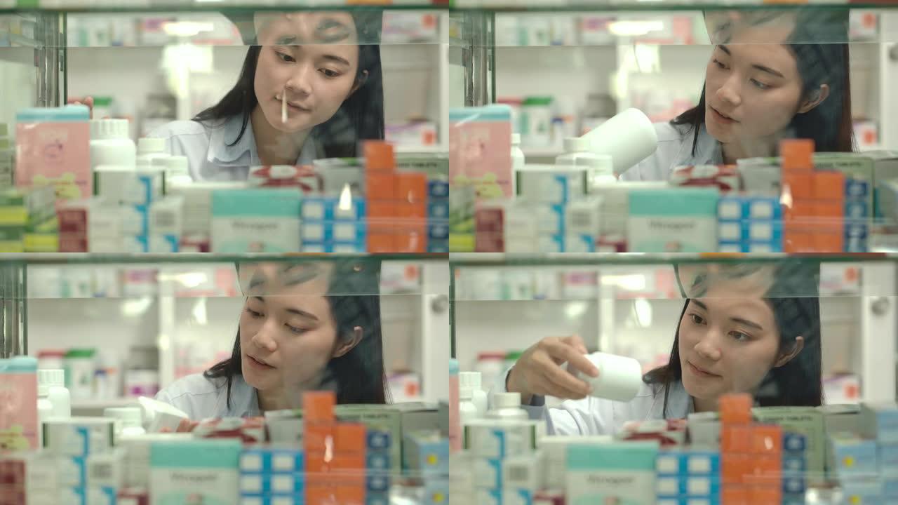 年轻的亚洲药剂师女人看着药房窗口中的药物。