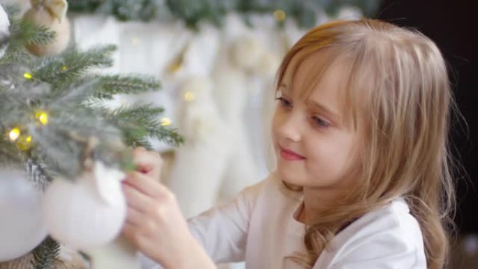 可爱的小女孩装饰圣诞树，对着镜头微笑