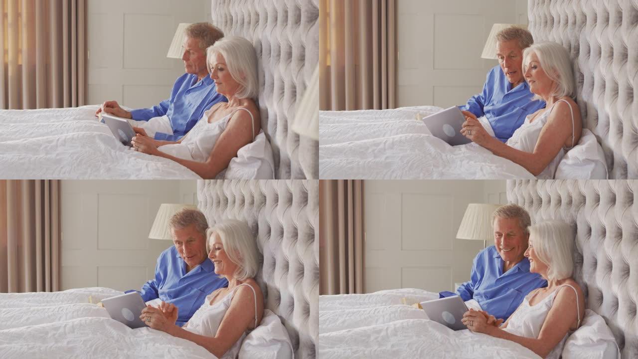 在Covid 19锁定期间，在家中的高级夫妇在床上用数字平板电脑自我隔离和阅读