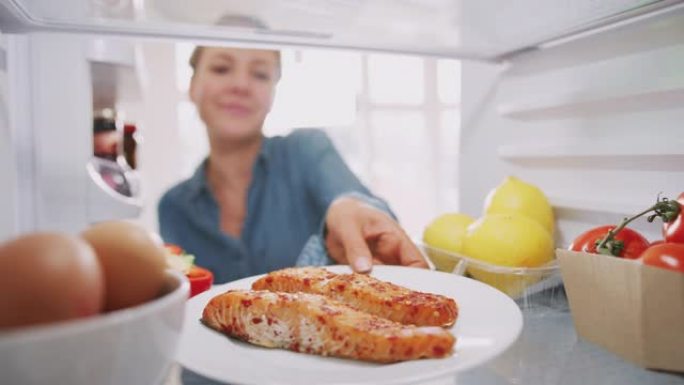 年轻女子将健康食品冰箱中的新鲜鲑鱼放在盘子里