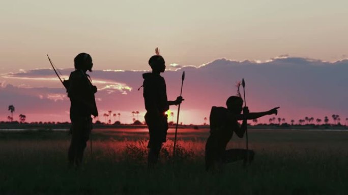 在博茨瓦纳的Makgadikgadi草原上，夕阳下三名桑族人/丛林人穿着传统服饰寻找动物的4K壮观的