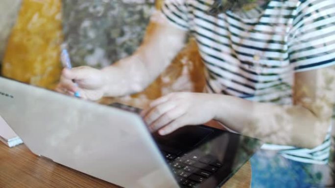 慢动作: 妇女使用笔记本电脑在笔记本上工作和书写，在家工作