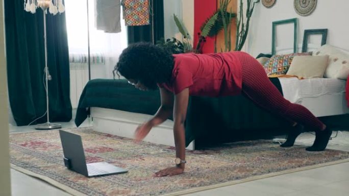 非洲女士正在用笔记本电脑在家锻炼。在家运动，在家健身的概念。