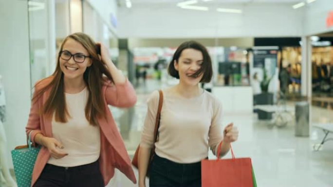 有吸引力的年轻女性正带着包走在购物中心，环顾四周，谈笑风生，享受着新的服装系列。
