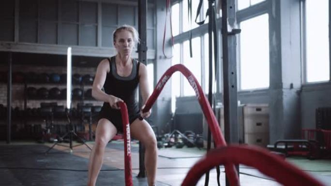 决心和耐力概念，年轻的运动高加索金发女子在大型健身房用战斗绳锻炼。