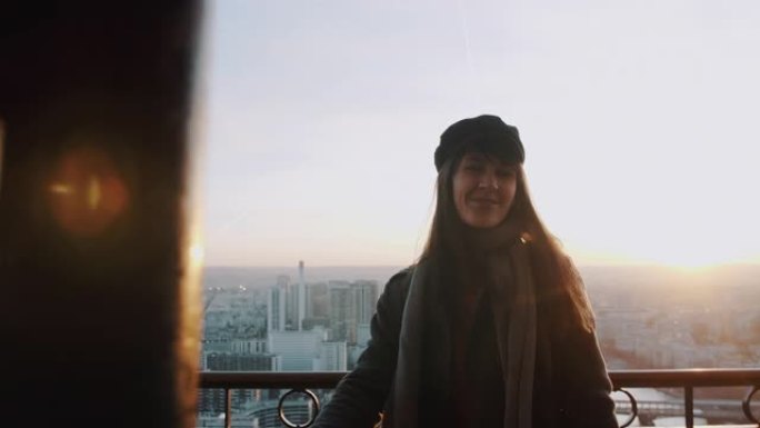 快乐美丽微笑的旅游女人靠在埃菲尔铁塔上的栅栏上，在日落天空背景慢动作上摆姿势。