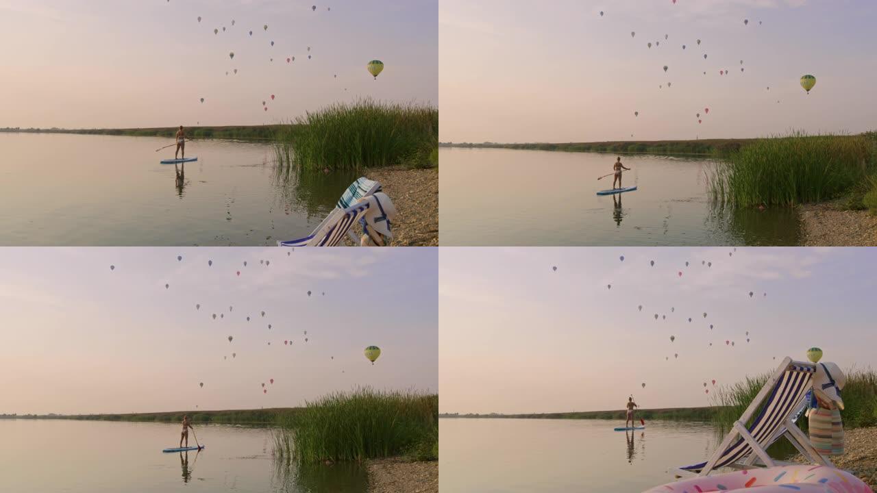 SLO MO女人划桨，而热气球在湖上飞行