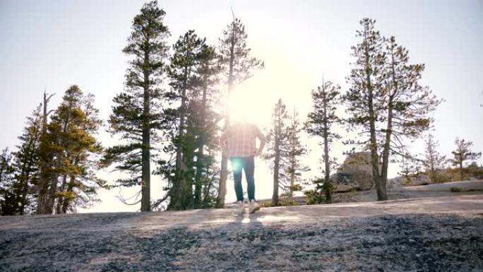 在优胜美地公园慢动作中，年轻人独自站在大石头上，太阳背光耀斑，令人惊叹的低角度拍摄。
