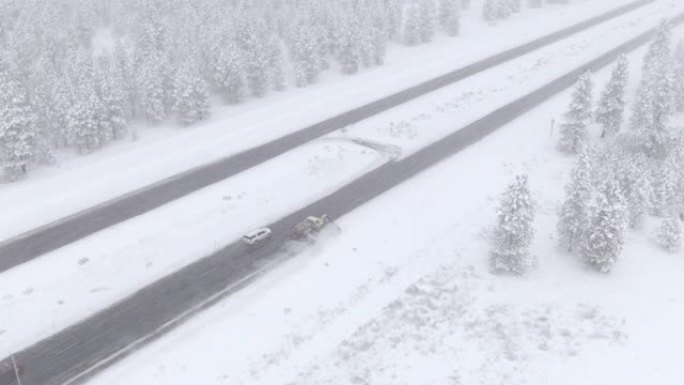 无人机: 扫雪机清除冰冷的高速公路时，在寒冷的常绿森林上方飞行